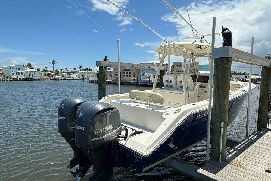 2015 Cobia 296 Center Console boat with twin Yamaha 300 engines docked by waterfront homes.