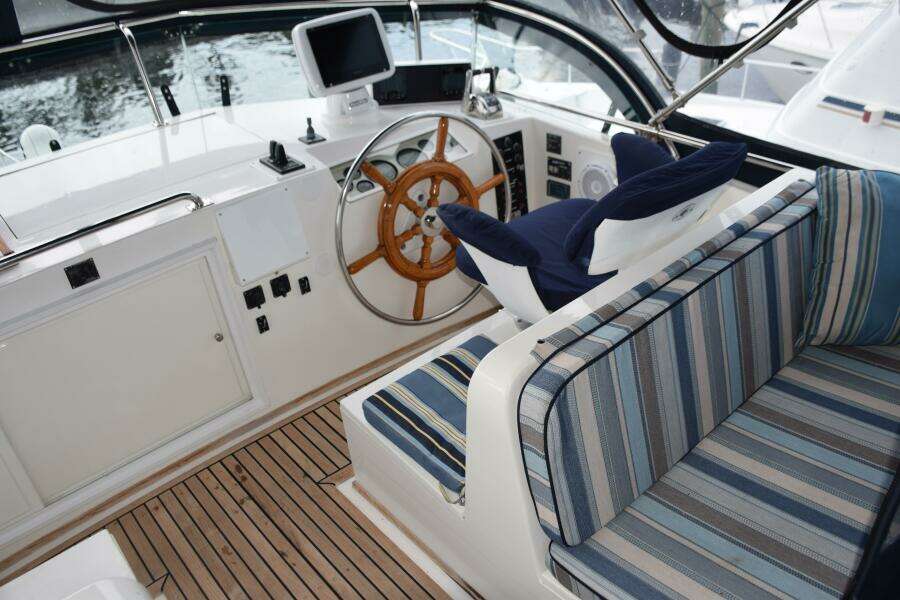 1997 Grand Banks Classic Yacht Helm With Striped Seating And Wooden Steering Wheel.